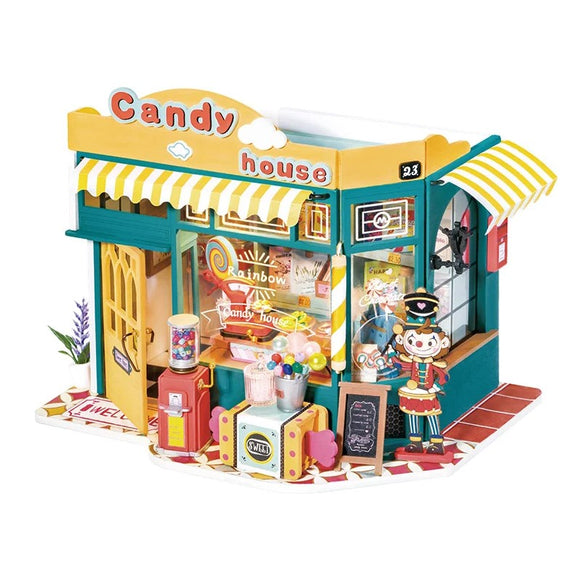 A colorful DIY kit featuring the Rainbow Candy House by Robotime. The vibrant model showcases a candy shop with a striped awning, decorative windows, and playful details. A whimsical figure of a candy seller stands outside, surrounded by candy jars and a vintage gas pump. The intricate design encourages creativity and hands-on building for enthusiasts.