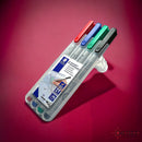 A transparent case containing four water soluble markers by Chessex, featuring red, blue, green, and black colors. Each marker is labeled and designed for easy grip, suitable for various art projects and games.