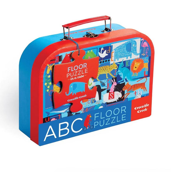 The Animal ABC Floor Puzzle by Crocodile Creek is packaged in a colorful suitcase-style box featuring various playful animal illustrations and bold colors. The box has a handle for easy transport and a prominent puzzle piece graphic that says 'FLOOR PUZZLE in a case'. It's a fun jigsaw puzzle designed for children to learn the alphabet through engaging animal images.
