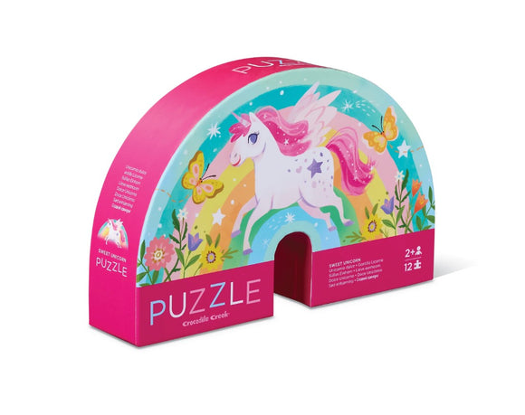 The Sweet Unicorn Mini Puzzle by Crocodile Creek features a whimsical design showcasing a colorful unicorn surrounded by butterflies and flowers. The puzzle is packaged in a vibrant pink box that is half-moon shaped, and it includes 12 pieces suitable for ages 2 and up, making it perfect for young children to enjoy.