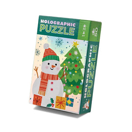 A vibrant and festive Holographic Snowman jigsaw puzzle box by Crocodile Creek. The illustration features a cheerful snowman wearing a colorful hat and scarf, standing in front of a decorated Christmas tree with presents underneath. Snowflakes fall in the background, creating a joyful winter scene. The puzzle is suitable for ages 4 and up, with 50 pieces.