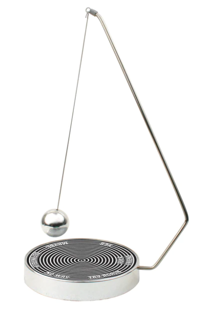 The Decision Maker by Kikkerland features a sleek metallic design with a pendulum ball on a springy arm. The base has a spiral pattern and labels indicating options like 'Yes', 'No', and 'Maybe', making it a playful tool for decision-making.