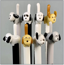 A collection of whimsical dog-themed gel pens from BC Mini. Each pen features a unique dog design on the top, showcasing various expressions and colors. The pens stand upright, with playful, cartoonish dog heads, including a black and white spotted dog, a golden retriever, and others with distinct features like glasses and happy faces, creating a delightful stationery set.