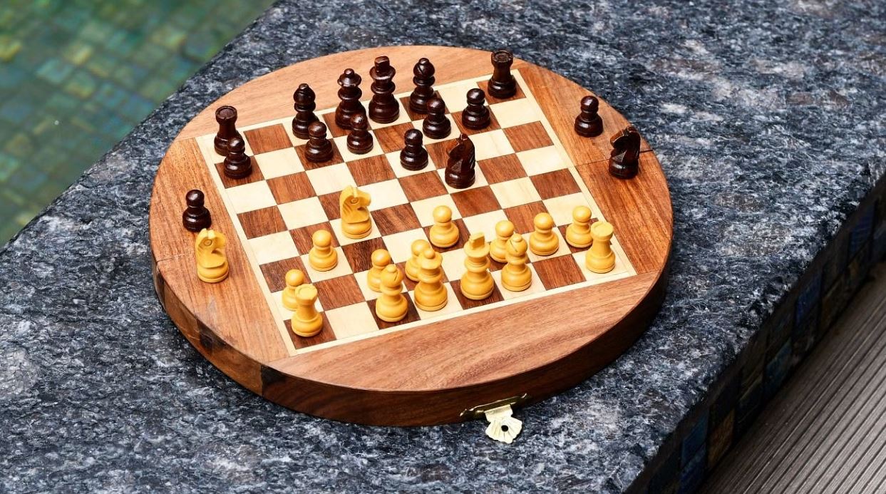 An elegantly crafted 9-inch round wooden chess set by R. Expo, featuring intricate wooden pieces in two contrasting colors positioned on a checkered board. The folding design allows for easy storage and transport, making it perfect for game nights and travel.