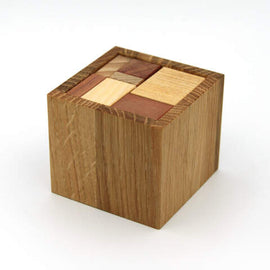 Coverho XS mechanical puzzle by VINCO, featuring a compact wooden cube design with a combination of different wood types inlaid on the top surface. The puzzle has a smooth, polished finish and a geometric pattern, designed to challenge the mind and enhance problem-solving skills. Perfect for enthusiasts of mechanical puzzles and brain teasers.