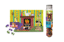 A colorful jigsaw puzzle featuring a cozy cat scene with a fireplace, adorned with various playful cats and decorations. Beside it is a tube containing the puzzle pieces, showcasing the vibrant design and inviting indoor atmosphere.