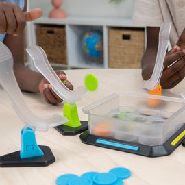 Two children engaging with the Flyfecta game by Fat Brain. The game features colorful launchers positioned above a clear container filled with discs. The players, focused and smiling, are about to launch discs into the container, showcasing a fun and interactive play experience.
