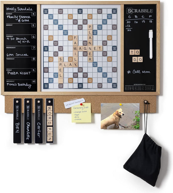 A Scrabble Message Center by Winning Solutions featuring a large Scrabble board, weekly schedule, and a corkboard section. The layout includes multiple words like 'FAMILY' and 'PLANNER' spelled out with wooden tiles, alongside a whiteboard for notes or to-do lists and a photograph of a dog. There are also grocery list notes pinned on the corkboard.