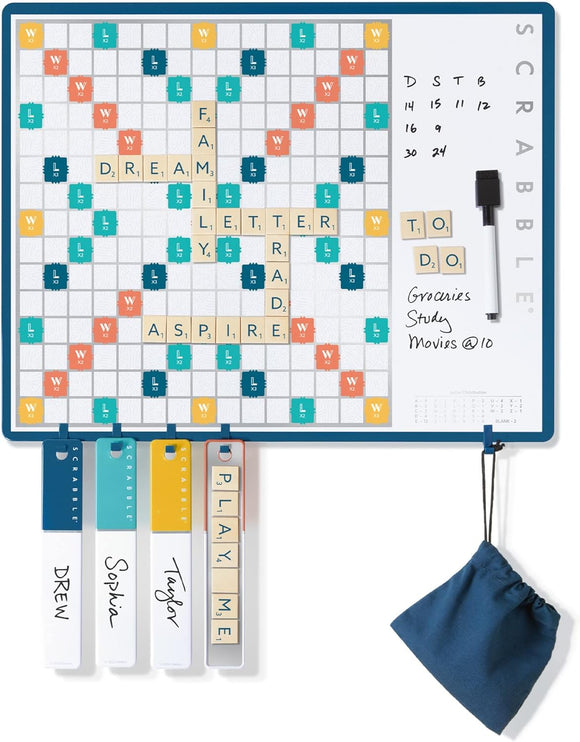 Scrabble 2-in-1 Message Board by Winning Solutions featuring a dual-use design. The game board displays words like 'FAMILY' and 'DREAM' with points, while also serving as a message board on the right. Includes letter tiles and a small fabric bag for storage, and clear markers for players' names.