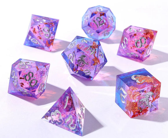 A beautifully crafted Gilded Storm Sharp Edge Dice Set featuring seven multi-faceted, resin dice in vibrant purple and pink hues with shimmering gold flakes. Each die displays intricate silver numbers and designs, suitable for tabletop games or role-playing sessions.
