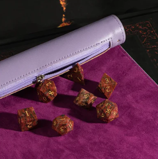 A stylish purple roll-up leatherette dice mat, featuring a textured surface ideal for tabletop games, with a matching zippered pouch beside it and various polyhedral dice resting on the mat. The mat is designed for easy transport and storage, making it perfect for gamers on the go.