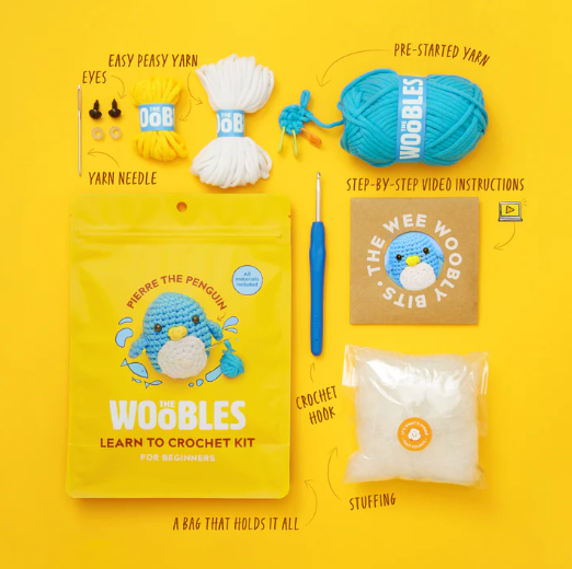 Penguin Beginner Crochet Kit by The Woobles includes colorful yarn, a yarn needle, a crochet hook, stuffing, pre-started yarn, eyes, and step-by-step video instructions. Everything is neatly packed in a bright yellow bag that holds all the supplies to create a cute penguin amigurumi.