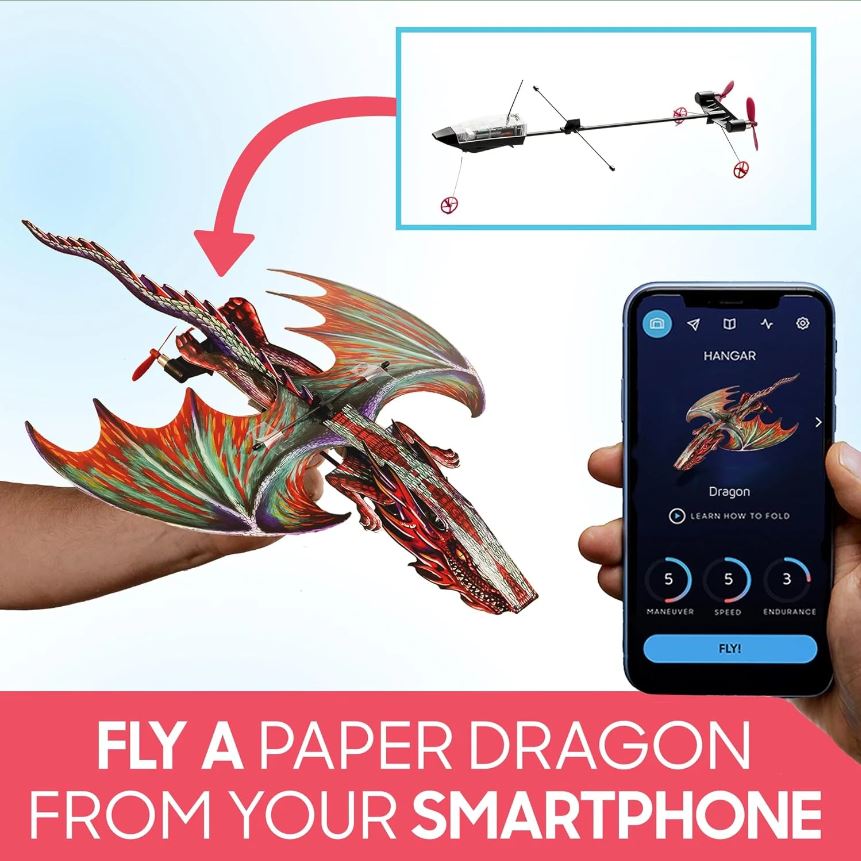 A person holds a colorful paper dragon model in one hand, while the other hand holds a smartphone displaying controls for flying the dragon. The dragon features vibrant colors and intricate designs, representing a fun and engaging DIY experience with a smartphone app integration.