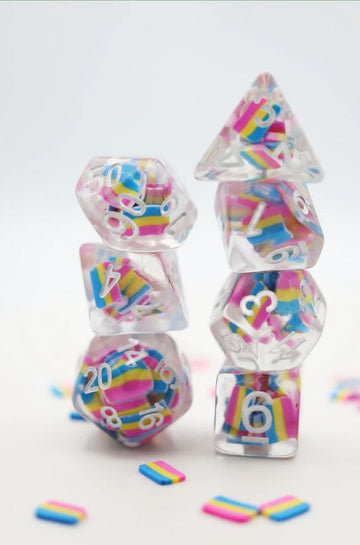 A colorful set of pansexual flag-themed RPG dice stacked creatively. The dice are clear with vibrant pink, yellow, and blue layers inside, showcasing their unique designs. Surrounding the dice are small, flat rectangular pieces in the same pansexual colors, enhancing the playful aesthetic.