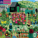 Colorful jigsaw puzzle featuring a vibrant garden scene with blooming flowers, a greenhouse, a black shed, and figures watering plants. The design showcases a variety of plants and gardening elements, set against a backdrop of rolling green hills under a blue sky. Ideal for puzzle enthusiasts and nature lovers.
