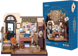 Mose's Detective Agency miniature model featuring a detailed office scene. The setup includes a wooden desk with a typewriter, a chair, a blue lamp, and a wall covered with investigation notes, maps, and photos. Accessories like a vintage telephone, a suitcase, and an umbrella stand are present, along with a decorative poster and a door leading outside.
