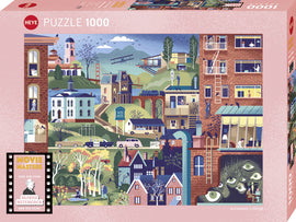 A colorful jigsaw puzzle box titled 'Movie Master, Hitchcock Films' by Heye, featuring a whimsical illustration depicting iconic scenes from Alfred Hitchcock's movies. The design includes various buildings, characters, and references to his films, inviting puzzlers to explore and assemble a 1000-piece challenge.