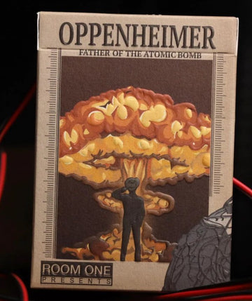 Oppenheimer Radiance Playing Cards by Room One, featuring a striking design influenced by the atomic bomb. The box depicts a figure standing before a nuclear explosion, showcasing vibrant orange and yellow colors. Ideal for card enthusiasts and collectors.