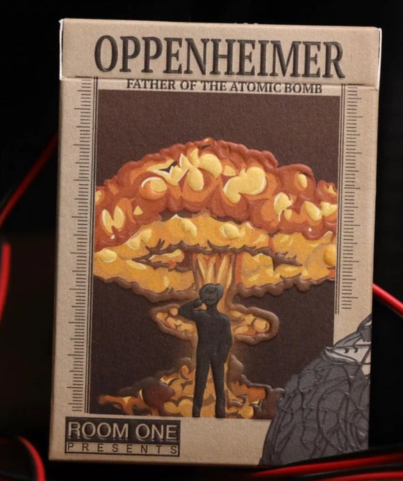 Oppenheimer Radiance Playing Cards by Room One, featuring a striking design influenced by the atomic bomb. The box depicts a figure standing before a nuclear explosion, showcasing vibrant orange and yellow colors. Ideal for card enthusiasts and collectors.