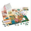 Joy Laforme Flower Shop jigsaw puzzle by Galison. The image shows a vibrant floral-themed puzzle depicting a charming flower shop setup. The puzzle pieces are scattered around the nearly completed puzzle, which features colorful flowers, potted plants, and decorative elements within a cozy flower shop setting. A whimsical puzzle box resembling a flower shop is positioned in the background.