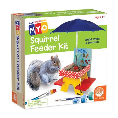 The MYO Squirrel Feeder Kit by MindWare features a colorful box showcasing a DIY kit for children aged 5 and up. The packaging displays a cheerful illustration of a squirrel and a small, red and yellow picnic-style feeder complete with an umbrella, along with paint and decorative elements. The text 'Build, Paint & Decorate' emphasizes its creative, hands-on approach for young crafters.