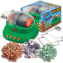 A vibrant green rock tumbler machine with a transparent lid, surrounded by various colorful gemstones in different sizes. The kit includes the tumbler itself, polishing powder, bags, and an AC adapter, all presented in a playful box designed for kids aged 8 and up.