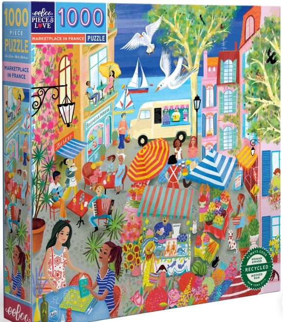 Eeboo's 1000-piece jigsaw puzzle titled 'Marketplace in France'. The vibrant artwork features scenes of a lively marketplace filled with people, colorful umbrellas, flowers, and quaint buildings. Residents engage in various activities, including dining, shopping, and music, all set against a sunny backdrop with boats and birds. The puzzle box showcases its intricate design and highlights the use of recycled materials.