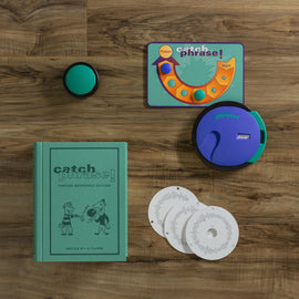 Catch Phrase Vintage Bookshelf game displayed on a wooden table. The set includes a green book cover with illustrations, a circular electronic device, a game board, and three circular cards.