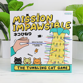 Mission Impawsible game by Gift Republic featuring a fun illustration of a hand removing colorful sticks from a tower. The game includes cute cat characters and instructions to avoid making the cats fall, making it ideal for family fun and gatherings.