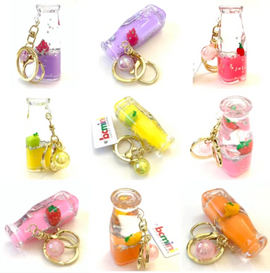 A colorful assortment of Fruit Float Bottle Keychains by BC Mini. Each keychain features a miniature bottle filled with vibrant liquids resembling fruit flavors, topped with decorative fruit pieces. The keychains are embellished with gold rings and charms, reflecting a playful and whimsical design suitable for all ages.