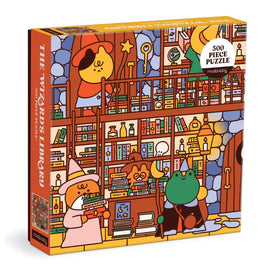 The Wizard's Library jigsaw puzzle by Mudpuppy featuring a whimsical illustration of various characters, including a wizard, a cozy frog, and a curious animal, set against a backdrop of colorful bookshelves filled with magical items. The box displays the title prominently along with a note indicating it contains 500 pieces.