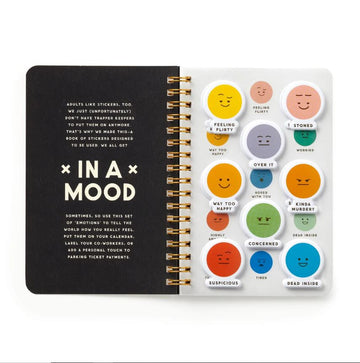 The 'In a Mood' sticker book by Brass Monkey, featuring a variety of expressive face stickers with moods like 'Feeling Flirty', 'Way Too Happy', 'Stoned', and 'Suspicious'. The book is designed to help adults communicate their emotions creatively, with a stylish black cover and gold spiral binding. Each page features colorful stickers that represent different moods, perfect for labeling calendars, sharing with coworkers, or adding a playful touch to various activities.