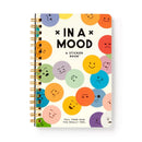 An open sticker book titled 'In a Mood' featuring a colorful cover with various emoji-style faces expressing different emotions. The book is spiral-bound, showcasing happy, sad, and neutral faces, inviting users to express their feelings creatively with stickers.