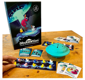 Abducktion: Base Game includes a colorful box featuring cartoon ducks and a UFO. The game setup displays a blue UFO toy, a game board with duck figures, and various play cards. A hand is reaching for a duck on the board.