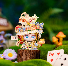 A vibrant model of Alice's Hat designed by Mu Model. Featuring intricate details, the model showcases playful elements like mini cards, cakes, and colorful embellishments. It stands on a wooden stump amidst a lush green background filled with flowers and whimsical mushrooms, capturing a magical, fairy-tale atmosphere.