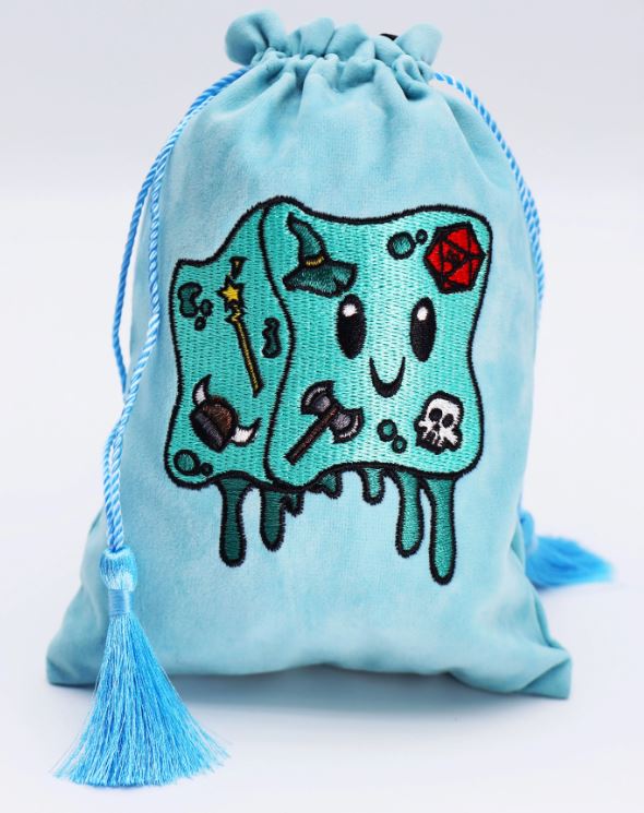 A cute, light blue dice bag from Foam Brain Games featuring a smiling gelly cube character. The bag is adorned with whimsical illustrations of a wizard hat, axe, gem, skull, and other playful designs. It has a drawstring closure with blue tassels hanging from it, making it perfect for storing dice or small gaming accessories.