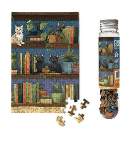 A Cat Tales Micropuzzle jigsaw featuring colorful illustrations of cats on a bookshelf surrounded by potted plants. Includes a clear tube with additional loose pieces.