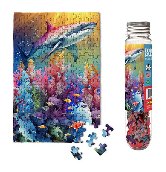 A vibrant jigsaw puzzle featuring marine life, including a shark swimming over colorful coral reefs and various fish. The puzzle pieces are shown scattered beside the puzzle image and the packaging, which is a clear tube featuring the same marine design.