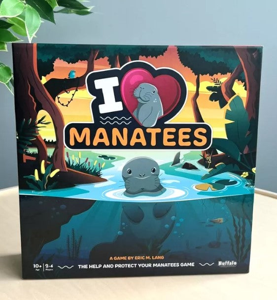 The I Heart Manatees game box by Buffalo Games features vibrant artwork of manatees in a serene water setting surrounded by lush trees. The title is prominently displayed with a heart symbol, emphasizing the theme of love for manatees. Suitable for ages 10 and up, the game supports 2 to 4 players.