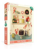 The packaging of the Devil's Food Cake jigsaw puzzle by New York Puzzle Company, featuring a vintage-style kitchen scene with a chocolate cake centerpiece, vibrant flowers, lobster motifs, and various bottles and jars on shelves. The puzzle contains 500 pieces and is designed for both adults and children.