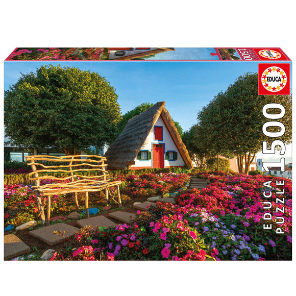 The Santana jigsaw puzzle by Educa features a picturesque scene of a charming thatched-roof house surrounded by vibrant flower beds and greenery. The image shows a rustic wooden bench, stone pathways, and a sunny blue sky, ideal for puzzle enthusiasts and nature lovers alike.