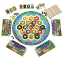 Catan: New Energies board game featuring a circular game board with hexagonal territories, resource cards, and various player pieces. The board is surrounded by player boards in different colors, and there are resource tokens and cards displayed on the sides of the board.