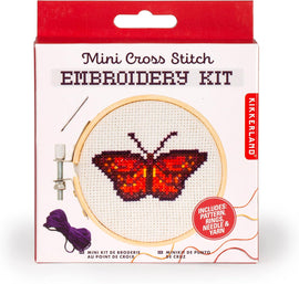 Kikkerland Butterfly Mini Cross Stitch DIY kit featuring a vibrant red butterfly design inside a wooden embroidery hoop. The packaging includes a needle, thread, and pattern instructions for easy crafting.