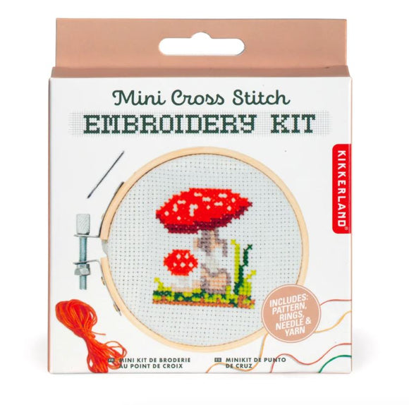 Mushroom Mini Cross Stitch Embroidery Kit by Kikkerland featuring a vibrant red and white mushroom design. The kit includes a pattern, rings, needle, and yarn for DIY cross stitching.