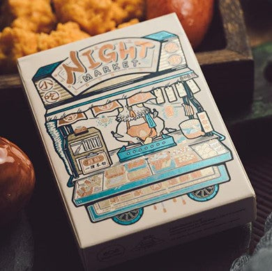 The Night Market: Day Playing Cards by 808 Magic & Bacon Magic features vibrant artwork showcasing a lively street food cart, adorned with intricate designs and colors. The box design reflects the fun and excitement of a night market atmosphere, ideal for card games and entertainment with friends and family.