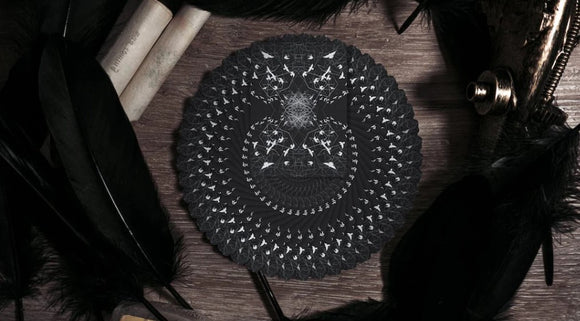 The Raven Black Dusk Playing Cards by WJPC featured on a wooden surface, surrounded by elegant black feathers and vintage scrolls. The cards display intricate black and white designs, making them a striking addition to any card game collection.