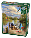 Cobble Hill 'Dog Day Afternoon' jigsaw puzzle featuring a scenic lakeside view. The puzzle box displays two dogs resting on a dock, surrounded by birds, a colorful sailboat, and lush greenery, showcasing a tranquil summer day.