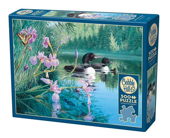 Cobble Hill 500-piece jigsaw puzzle titled 'Iris Cove Loons'. The box features a serene image of two loons swimming in calm water, surrounded by vibrant purple flowers and a butterfly. The background includes lush greenery and reflections on the water, beautifully illustrating a tranquil natural setting.