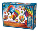 A Cobble Hill jigsaw puzzle titled 'Up in the Air' featuring a colorful scene of hot air balloons soaring above a desert landscape. The box contains 500+ pieces and includes a poster for reference. The vibrant balloons come in various patterns and colors, creating a cheerful and whimsical atmosphere.