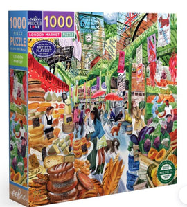 Colorful jigsaw puzzle titled 'London Market' by Eeboo, featuring a bustling market scene with various vendors selling fruits, vegetables, baked goods, and people shopping. The illustration captures the vibrant atmosphere of a London market with detailed imagery, including signs, umbrellas, and multiple market stalls.